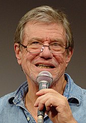 Director John McTiernan dressed in a blue shirt and glasses facing the camera