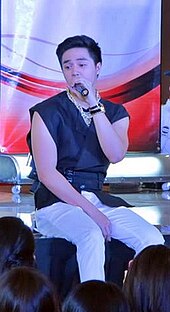 An image of Sam Concepcion sitting onstage while singing