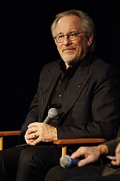 Steven Spielberg sits on a chair with a microphone in his hand