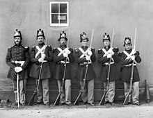 black & white photograph of six U.S. marines standing in line, five with Civil War-era rifles and one with an NCO sword.