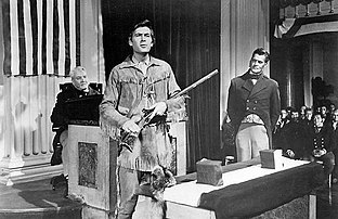 Man dressed as Davy Crockett with a rifle in his hand, alongside two men in the background