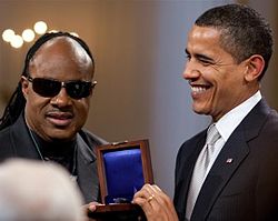Barack Obama smiling and holding a medal and presenting it to Wonder