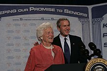 Barbara Bush and George W. Bush stand in front of a backdrop reading "Keeping Our Promise to Seniors"