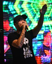 Close-up image of Chito Miranda wearing a cap and singing to a hand held mic