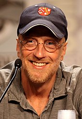 Un homme souriant portant une casquette et des lunettes.