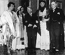 photograph of Carl Nielsen in a suit linking arms with costumed members of the cast of Saul and David