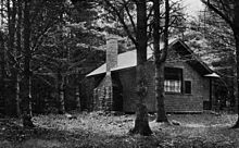 Star Studio in the woods, showing the side with the chimney and the side with a window with curtains