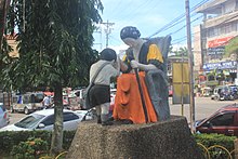 Colored outdoor statue of a child pressing their forehead on the hand of a seated elder