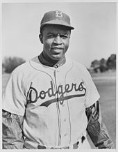 A black man in a Brooklyn Dodgers uniform and a cap with the letter "B", smiling at the camera.