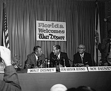 Three men at a table with microphones in front of them announcing something