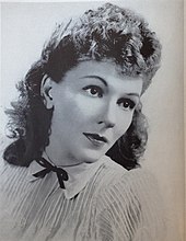 Portrait of a woman in her mid-thirties, with long curly hair and wearing an old-fashioned blouse with string tie