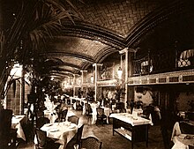 Historical view of the basement's double-height grill room. The space has a vaulted ceiling, as well as an elevated gallery behind a set of columns to the right.