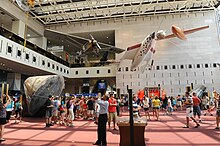 Patrons mill around hall with SpaceShip One, the Spirit of Saint Louis, and the Apollo 11 command module