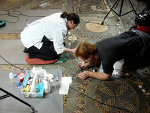 Two conservators kneeling on the Cosmati pavement, surrounded by conservation and cleaning tools