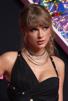 Swift wearing a black cocktail dress with asymmetrical top and multiple necklaces.
