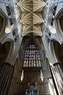 The inside of Westminster Abbey's nave, with a high vaulted ceiling and large stained-glass window at the end.