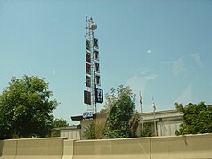 A one-story building with a microwave tower on which five square signs are hung, with the letters K, T, V, and T, and the CBS 11 logo. A smaller UPN 21 sign adorns the front of the building.