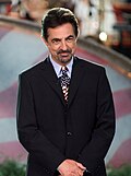 A man with a black-grey goatee in a black suit with an American flag tie