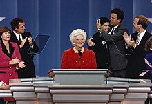 Bush stands smiling in front of a lectern with her family standing behind her