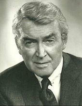 A sepia-toned headshot of a silver-haired Stewart in a suit