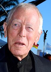 A profile image of Max von Sydow. An elderly Caucasian man with short white hair. He is facing forwards while looking off to the left, with a slight, open-mouthed smile.