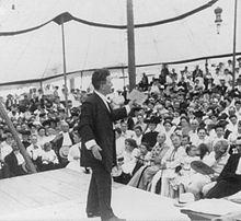 La Follette addressing a crowd of hundreds of people from a stage.