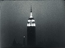 Grainy, black-and-white still frame of the illuminated Empire State Building against the night sky