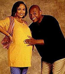 a bald man stands with his pregnant wife.