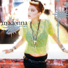 Madonna standing on a bridge wearing a light green see-through top, a bridal mini-veil and black pants.