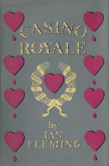 A book cover: down the left and right sides are representations of hearts, four on each side, each one with a drop of blood below them. In the centre of the image is another heart but without the blood drop. This central heart is surrounded by a gold laurel leaf bearing the words "A whisper of Love, A Whisper of Hate". Above the heart / laurel is the title, Casino Royale; below the heart / laurel are the words "by Ian Fleming"
