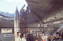 Large, underground missile silo with a missile pointing out the hole toward the sky next to a support structure. Five characters stand in the foreground.