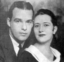 Head and shoulders of a young white man and woman, with their faces close together, looking toward the camera, in studio portrait