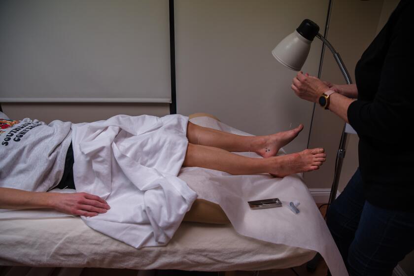 Tracey Whitney places acupuncture needles on Rachael Lackner's legs in Poway on March 1, 2021.