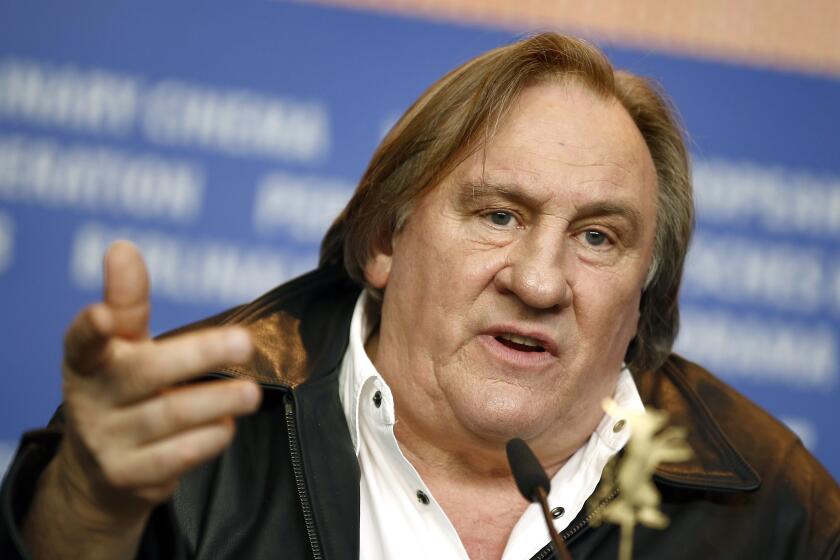 Actor Gerard Depardieu leans and points his finger as he speaks into a small microphone