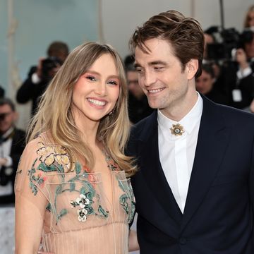 suki waterhouse and robert pattinson attend the met gala 2023, she's wearing a see through nude dress with floral embroidery on the bodice and he's wearing a white shirt with a golden brooch and a black jacket