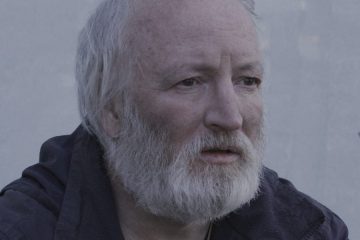 An old man with a white beard stares off into the distance