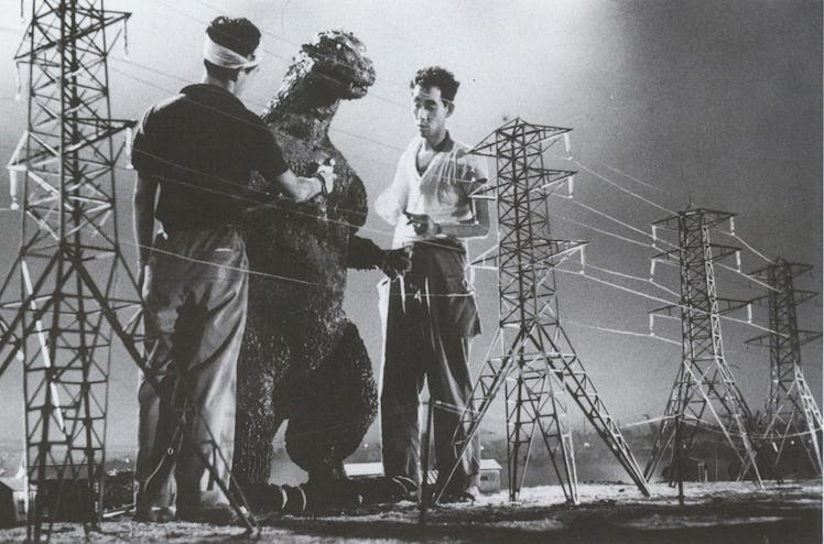 Godzilla ‘full-size’ man-in-suit performer standing next to miniaturized buildings