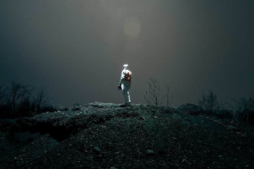 A person stands in a white hazchem suit on the top of a hill