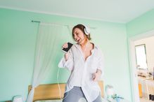 Young woman on bed wearing headphones and singing into smartphone