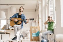 Horrified son covering his ears with father playing guitar at home