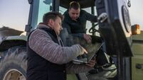 Man with short brown hair,pointing on his laptop while standing next to his colleague,colleague sitting inside his tractor and l
